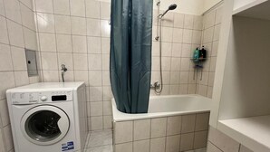 Une salle de bain équipée d’un lave-linge, d’une baignoire et d’une douche.