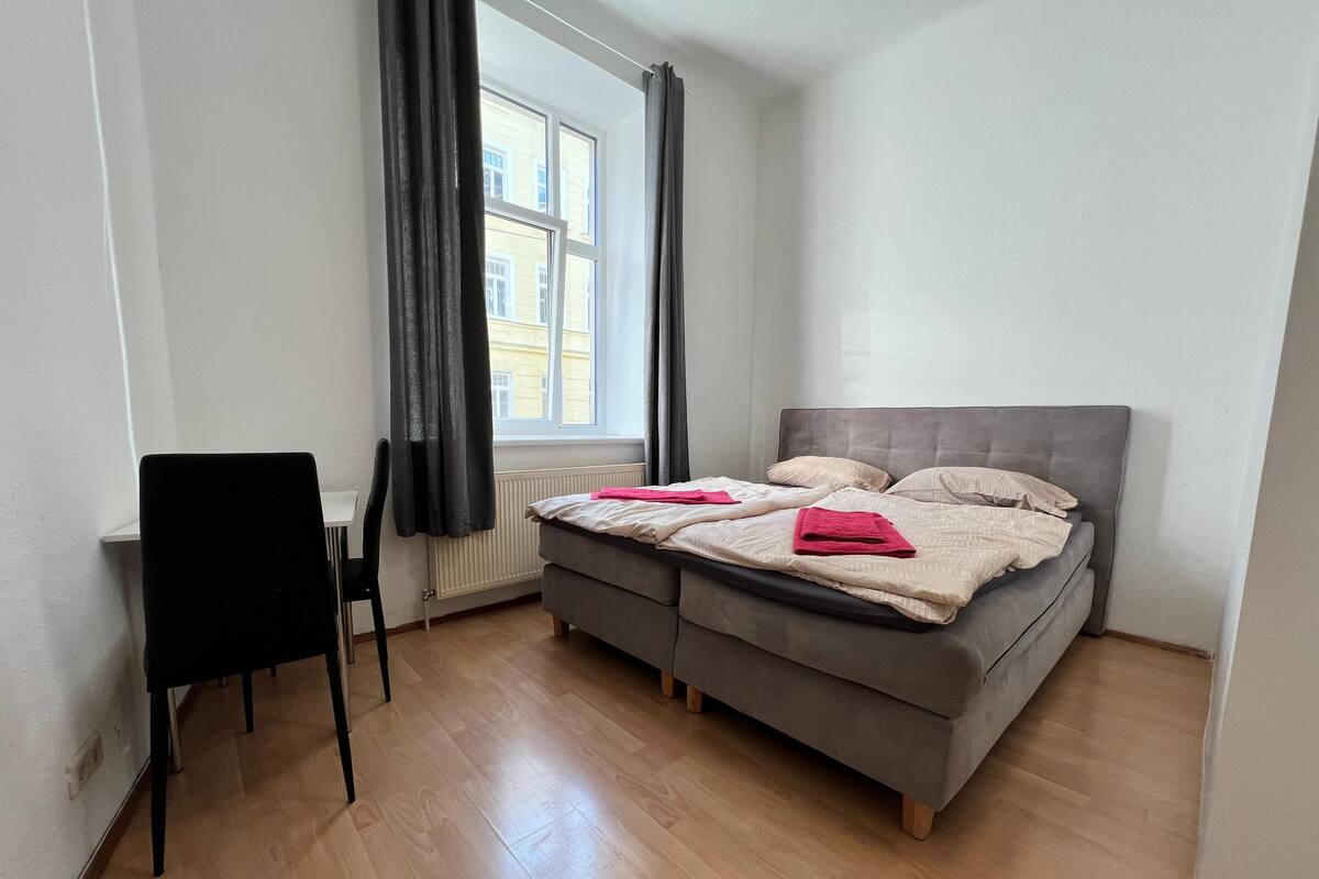 A bedroom with a bed, a chair, a desk, and a window.