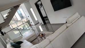 Una sala de estar moderna con un sofá de cuero blanco, una mesita redonda y un televisor montado en la pared.