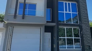 Una casa moderna de dos pisos con garaje, ventanas grandes y fachada de piedra.