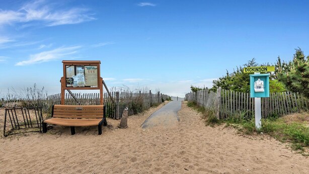 Een zandpad aan het strand met een houten bankje en een bordje met de tekst 'Dickinson'.