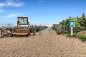 Un sentier de sable bordant la plage, avec un banc en bois et un panneau indicateur portant l’inscription « Dickinson ».