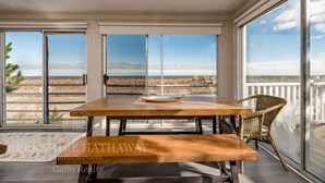 Comedor con mesa de madera y bancos, ventanas amplias con vistas a un paisaje desértico y sillas de mimbre.