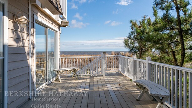 Terraza de madera con banco y mesa, con vista a una playa y el océano.