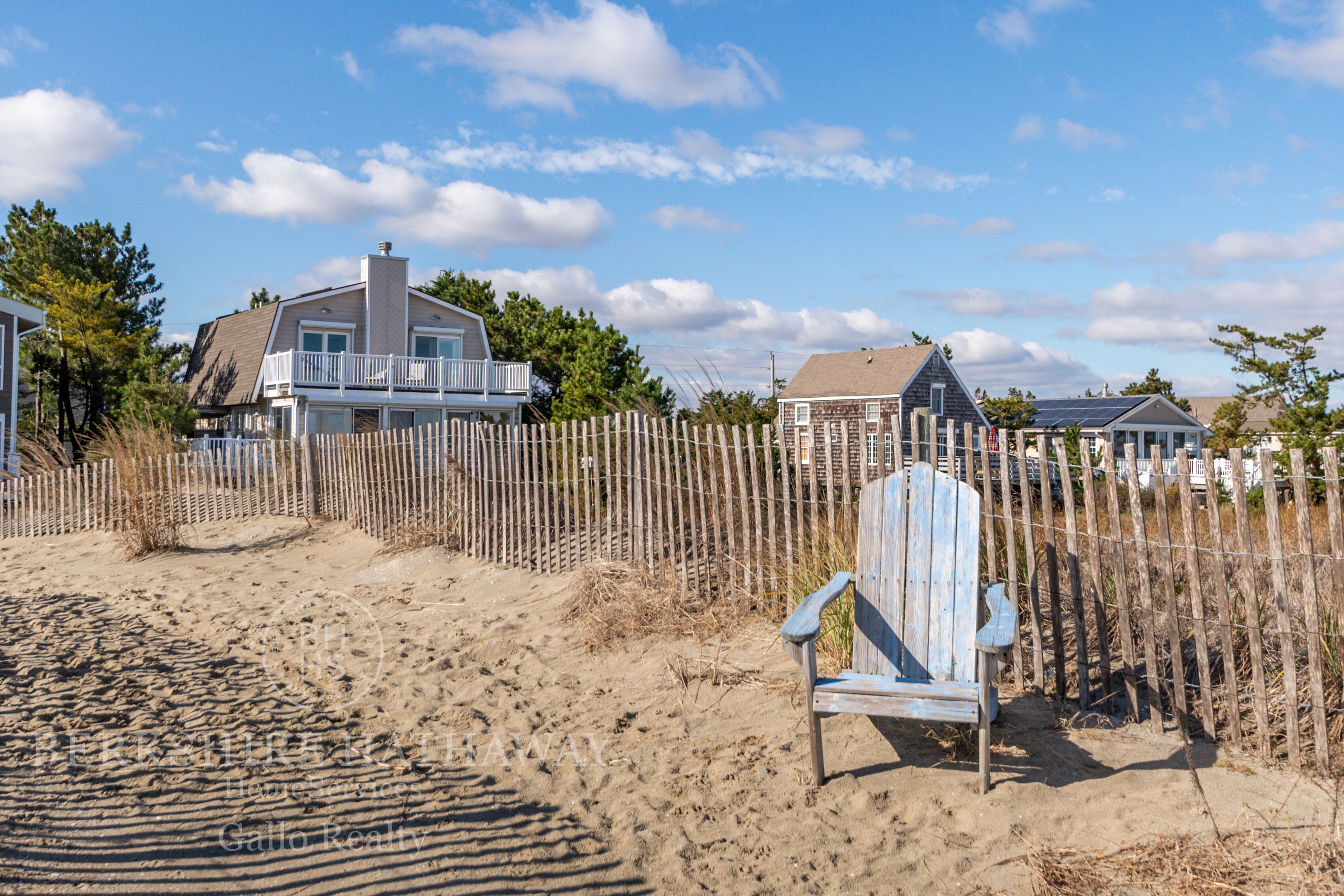 Una casa de playa con valla de madera, una silla y cielo despejado.
