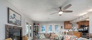 A spacious living room with a large sectional sofa, a glass coffee table, and a fireplace. There is a kitchen area with wooden cabinets and modern appliances. - Bayfront home on Broadkill Beach!  1412 S Bayshore (Milton)