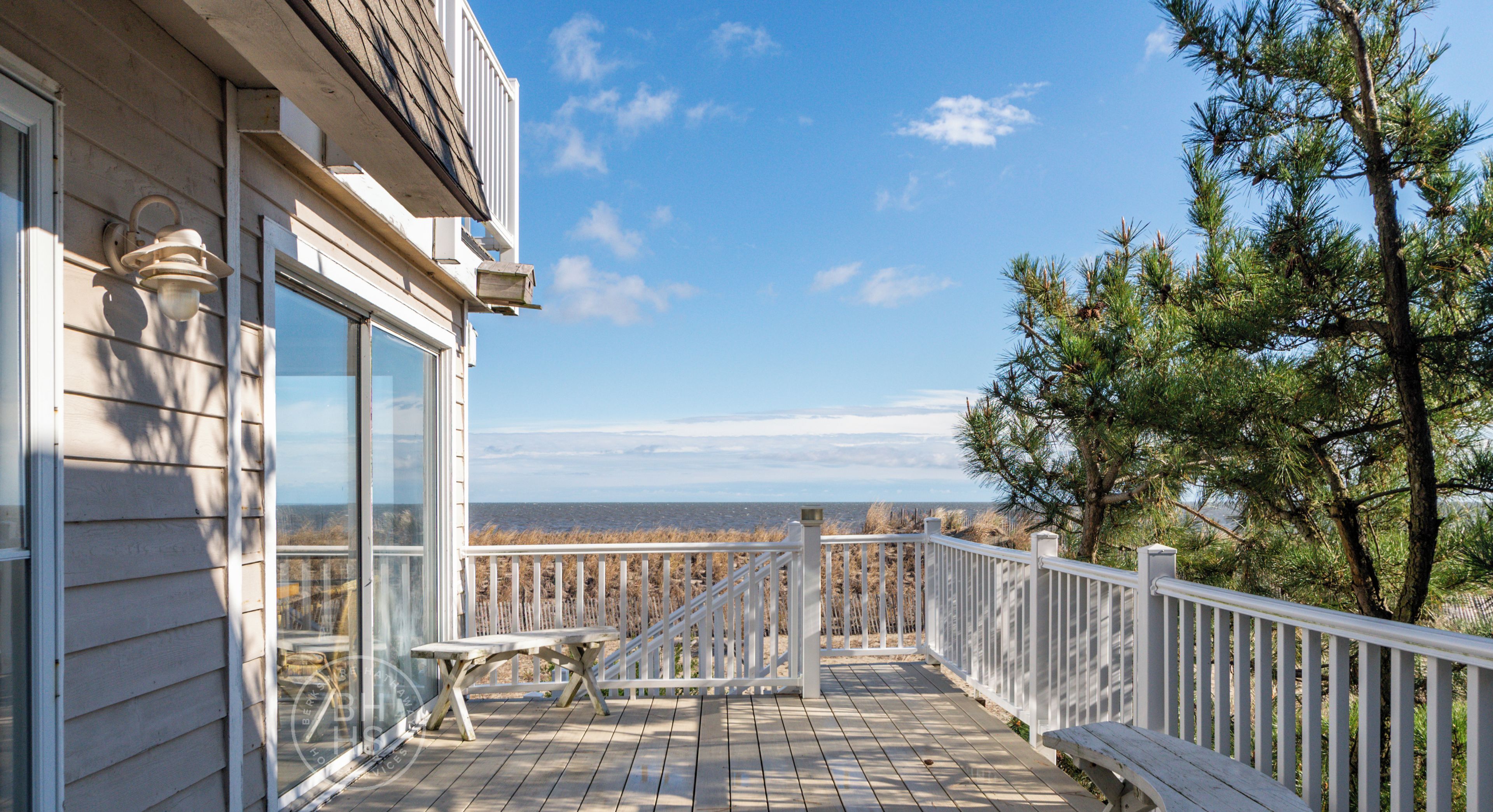 A wooden deck with a bench and a table, overlooking a beach and ocean.
