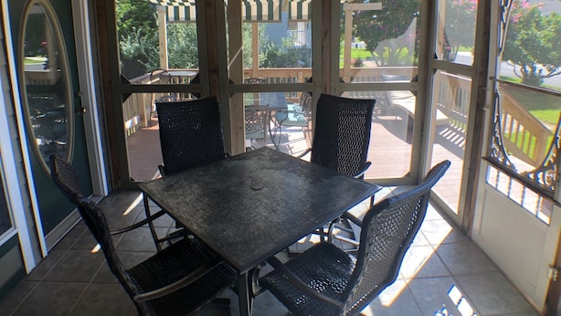 A covered patio area with a table and chairs, wooden ceiling beams, and a view of the outdoors.