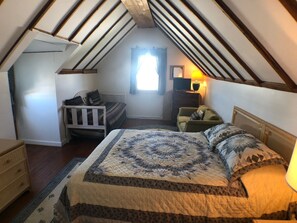 A cozy attic bedroom with a large bed, a small desk, and a chair.