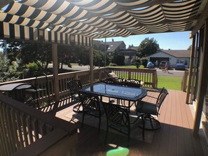 A covered outdoor deck with a glass-top table and chairs, surrounded by a wooden railing.