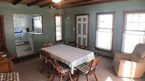 A dining area with a table and chairs, a kitchen in the background, and a ceiling fan.