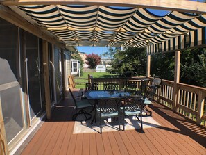 A covered patio with a table and chairs, wooden railings, and a view of the backyard.