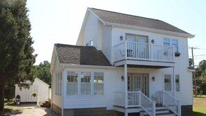 A two-story white house with a front porch, a balcony on the upper floor, and a small attached garage. - Just a block to the beach!  701 Cedar (Lewes)
