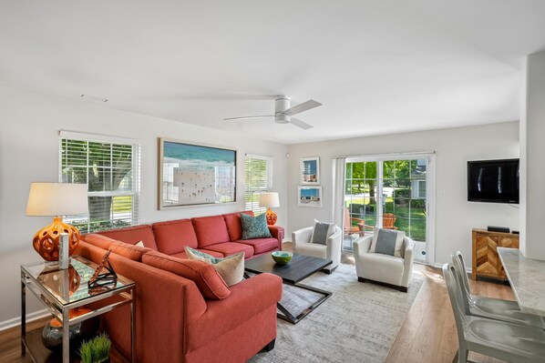 A living room with a red sofa, white armchairs, a glass coffee table, and a ceiling fan. - 1 Kendall Lane, Villas At Eagles Landing, Rehoboth Beach, Delaware (Rehoboth Beach)