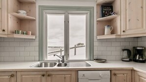 A kitchen with a double sink, wooden cabinets, a dishwasher, and a window with a view of a snowy landscape. - Seaside Bliss for Families: Home Away from Home (Stockholms län)