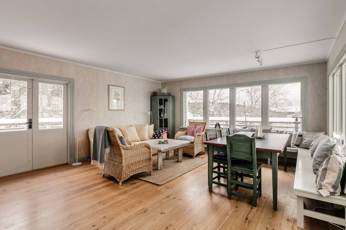 Un salon spacieux doté d’un plancher en bois, d’un canapé, d’une table à manger avec des chaises, et offrant une vue dégagée grâce à de grandes fenêtres.