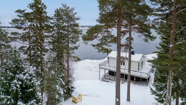 A cabin with a deck overlooking a lake, surrounded by tall trees. - Seaside Bliss for Families: Home Away from Home (Stockholms län)