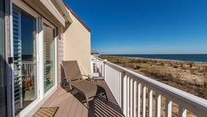 A balcony with two chairs and a table, overlooking a beach with dunes and the ocean.