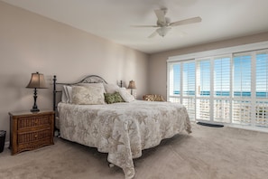 A bedroom with a bed, two bedside tables, a ceiling fan, and a large window with a view.