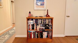 Een boekenplank met verschillende boeken en een miniatuur van een vuurtoren, een lijst met foto en een bord erboven.