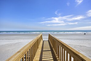 A wooden boardwalk leading to a beach with a clear sky.