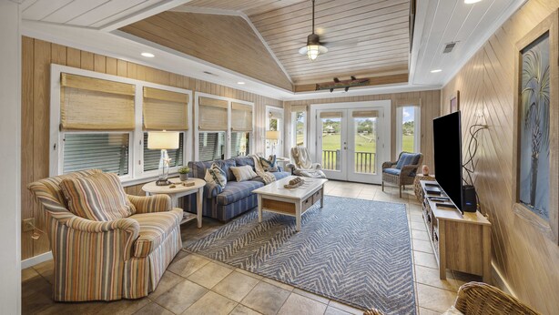 A spacious living room with a large sofa, striped armchair, and a coffee table. There is a television on a wooden stand, and a large window with blinds. - Peace of Pawleys - Creek Front, 3-bedroom (Pawleys Island)
