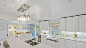 A modern kitchen with white cabinetry, a long island with a sink, and a hanging light fixture. - Peace of Pawleys - Creek Front, 3-bedroom (Pawleys Island)