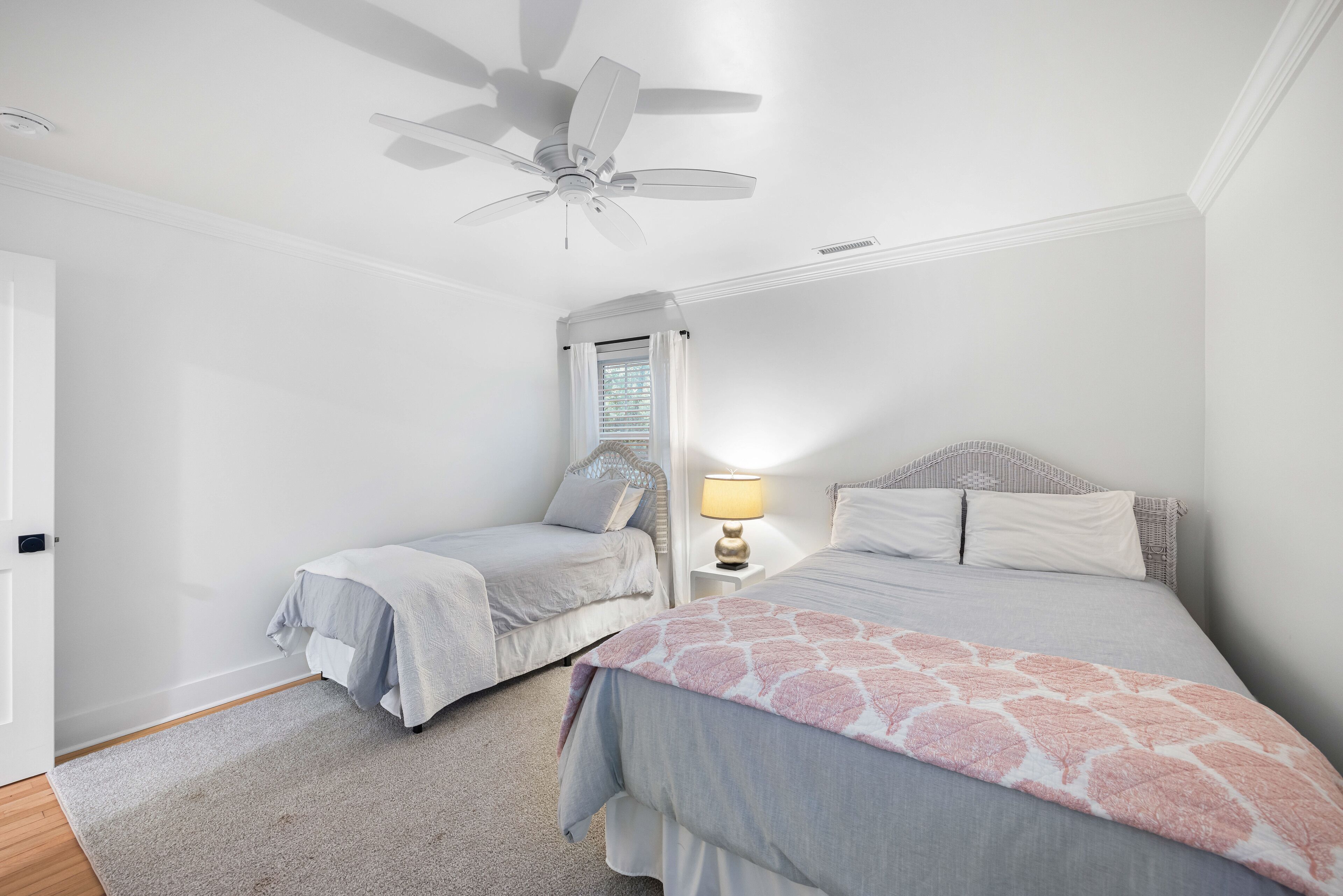 A bedroom with two single beds, a ceiling fan, a nightstand with a lamp, and a window with curtains.