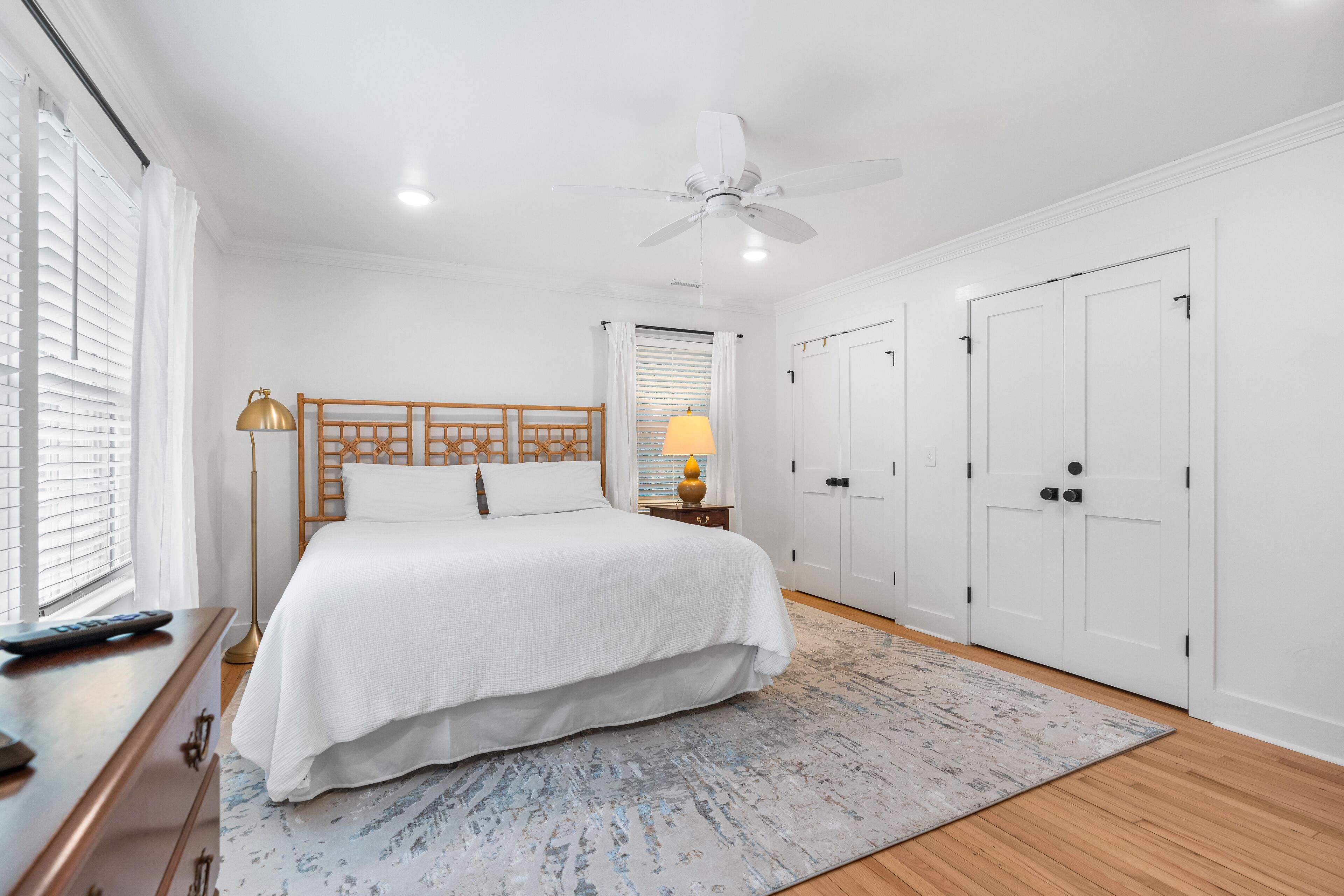 A bedroom with a large bed, a ceiling fan, white walls, and a wooden floor.