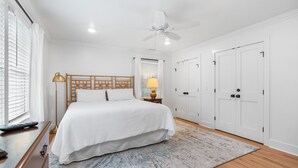 Ein Schlafzimmer mit einem großen Bett, einem Deckenventilator, weißen Wänden und einem Holzboden.