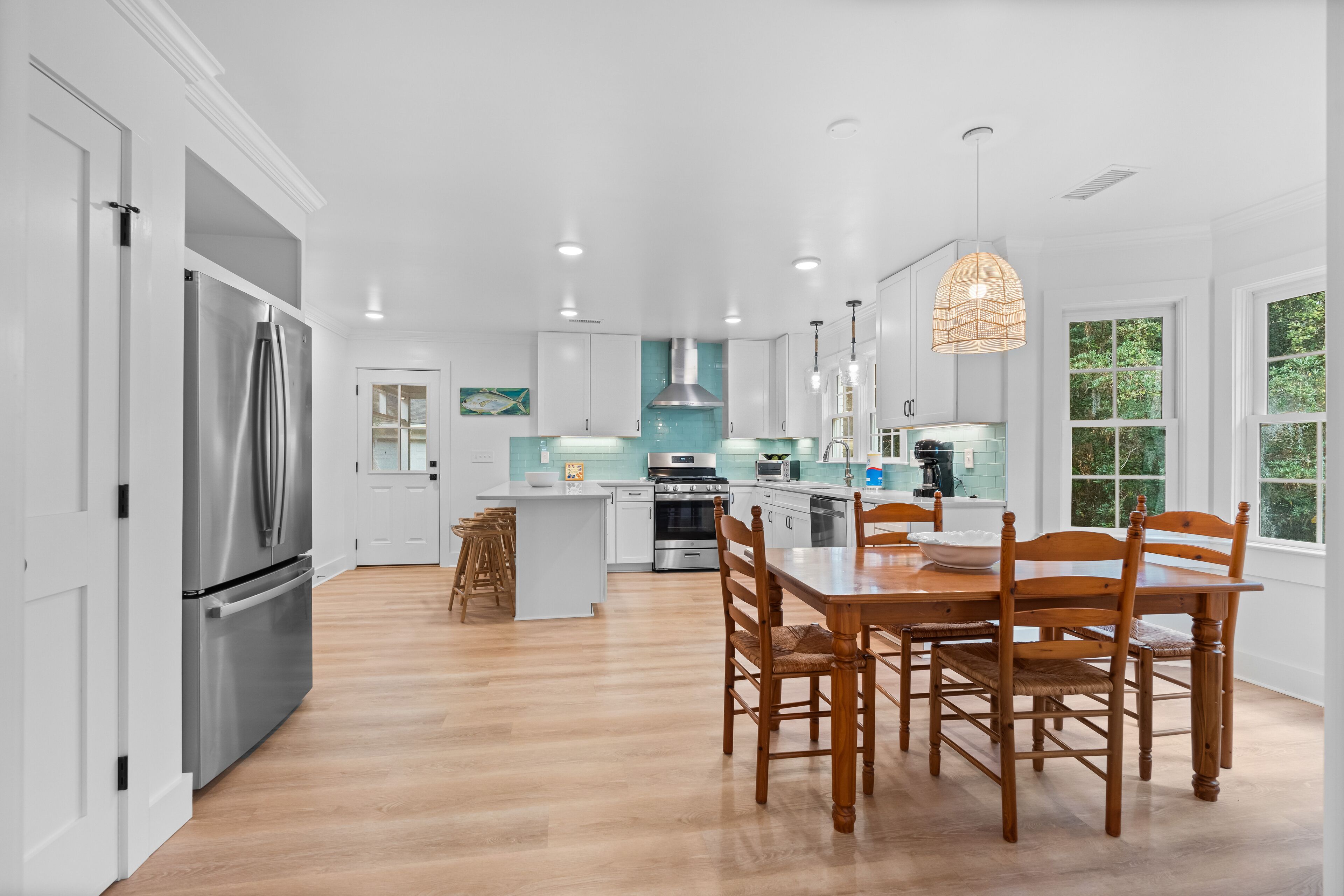 A modern kitchen with white cabinetry, stainless steel appliances, and a wooden dining table.