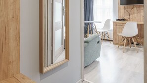 A modern hotel room with a wooden door, a mirror, a desk with a chair, a television, and a view into the dining area. - RentPlanet - Apartament Kiełbaśnicza (Wroclaw)