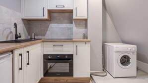 A compact kitchen with white cabinets, a built-in oven, and a washing machine. - RentPlanet - Apartament Kiełbaśnicza (Wroclaw)