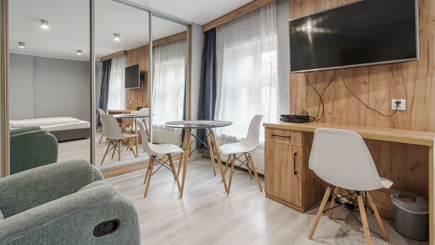 A modern room with a wooden desk, a flat-screen TV, a round dining table with chairs, a sofa, and a large mirror. - RentPlanet - Apartament Kiełbaśnicza (Wroclaw)