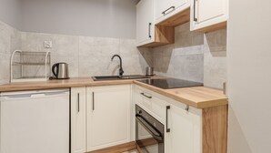 A modern kitchen with white cabinets, a wooden countertop, a dishwasher, an oven, and a sink. - RentPlanet - Apartament Kiełbaśnicza (Wroclaw)