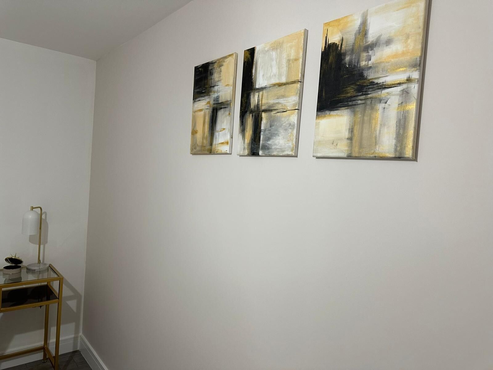 A room with three abstract paintings on the wall, a small table with a lamp, and a floor lamp.