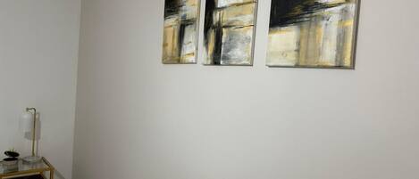 A room with three abstract paintings on the wall, a small table with a lamp, and a floor lamp.