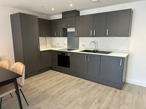 A modern kitchen with dark cabinets, a black oven, and a sink. - The Nest 1-bed Apartment in Hemel Hempstead (Hemel Hempstead)