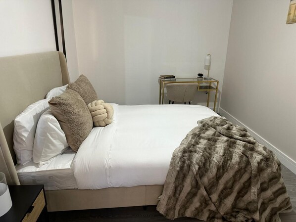 A neatly made bed with white linens and a large, fluffy throw blanket. There is a small bedside table with a lamp and a book. - The Nest 1-bed Apartment in Hemel Hempstead (Hemel Hempstead)