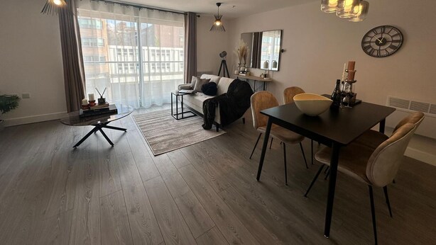 Un salon moderne avec un canapé, une table à manger et des chaises. On y trouve une grande fenêtre avec des rideaux, un lampadaire et une horloge murale.