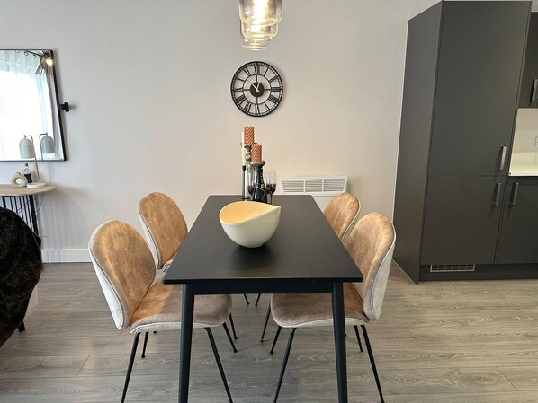 Un comedor con una mesa negra, seis sillas, un cuenco blanco, un reloj de pared y una lámpara colgante moderna.