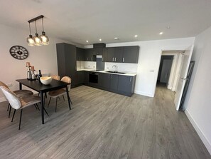 A modern kitchen with dark cabinets, a white countertop, and a dining area with a table and chairs. - The Nest 1-bed Apartment in Hemel Hempstead (Hemel Hempstead)