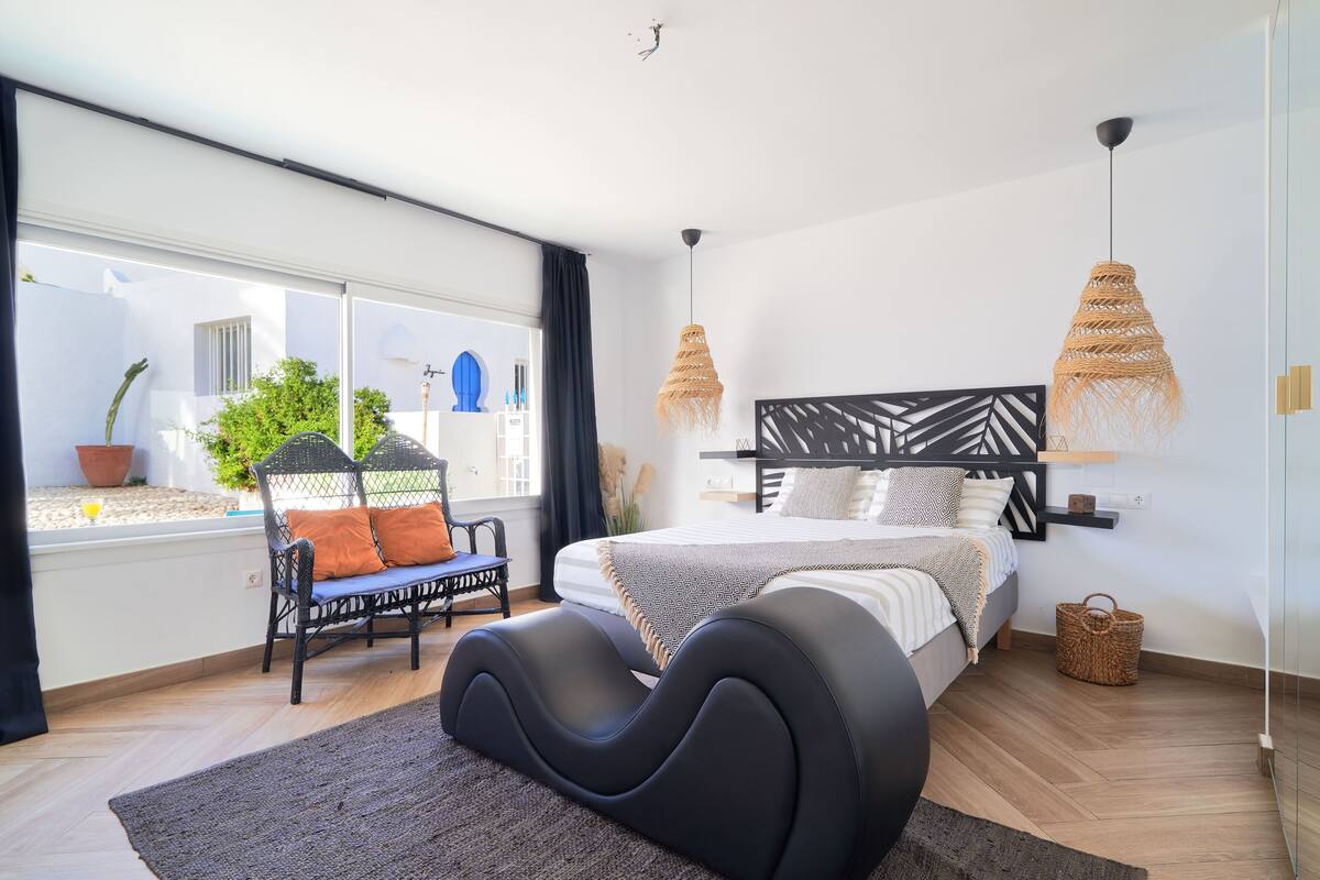 A modern bedroom with a bed, a chair, a large window, and a view of the outside.