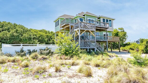 Ein mehrstöckiges Strandhaus mit einer Holzterrasse und Treppen, die zu den oberen Stockwerken führen.