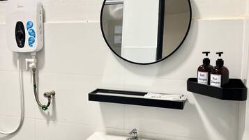 A bathroom with a white sink, a mirror, a handheld showerhead, and a shelf with two bottles of shampoo.
