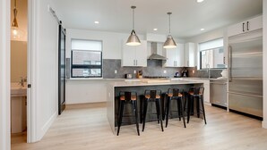 A modern kitchen with a central island, bar stools, pendant lighting, and a large refrigerator. - US1211 | Modern Interiors | A/C | Roof Top Hot Tub (Steamboat Springs)