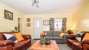 A living room with two brown leather sofas, a wooden coffee table, and a grey sofa. There are framed pictures on the walls and a door in the background.