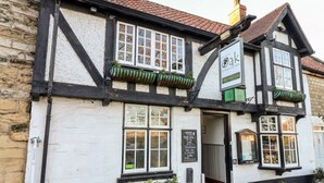 A traditional pub with a white facade and black timber framing. It features multiple windows with green flower boxes and a sign indicating it is a pub and restaurant.