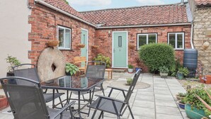 A patio with a glass table and chairs, a brick house with a green door, and potted plants.