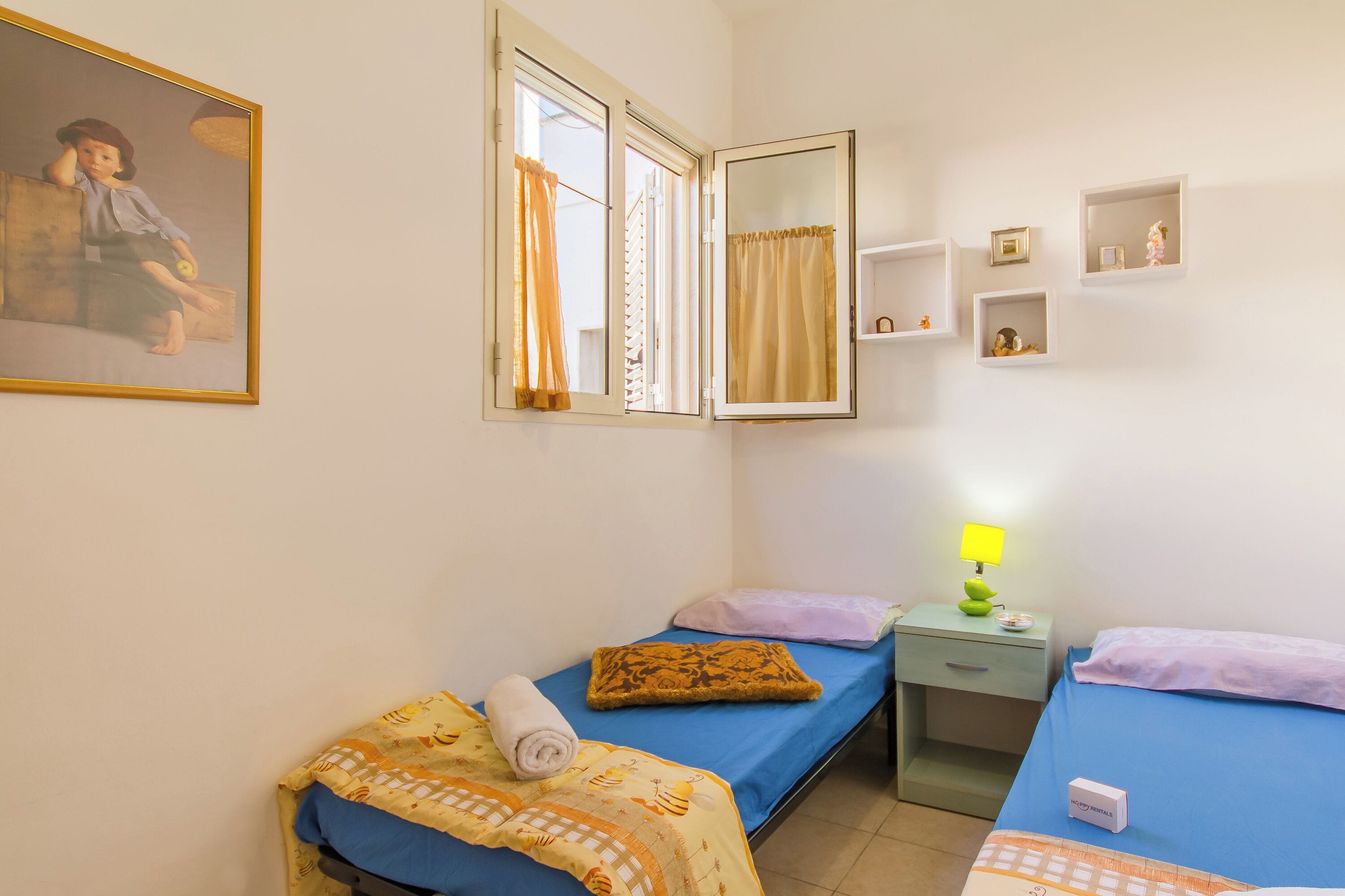 Una habitación con dos camas, una mesita de noche, una lámpara y un cuadro en la pared.